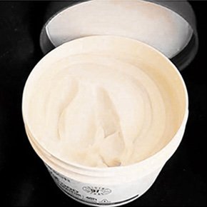 Open tub of creamy product on black surface