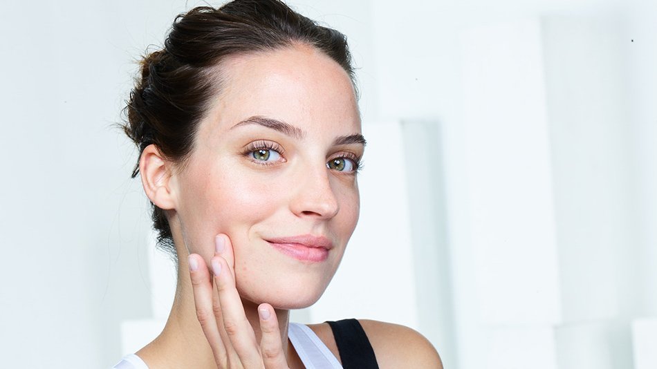 Woman with hair up touching her face in a brightly lit room